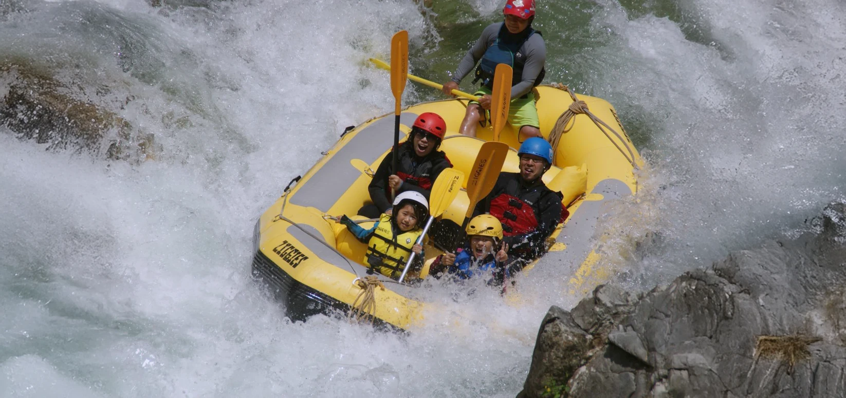 家族で楽しむみなかみラフティング。日本の激しいホワイトウォーター急流を黄色いボートで下るアドベンチャーツアー,Family Minakami rafting in Japan riding a yellow raft through powerful whitewater rapids on an adventure river tour.
