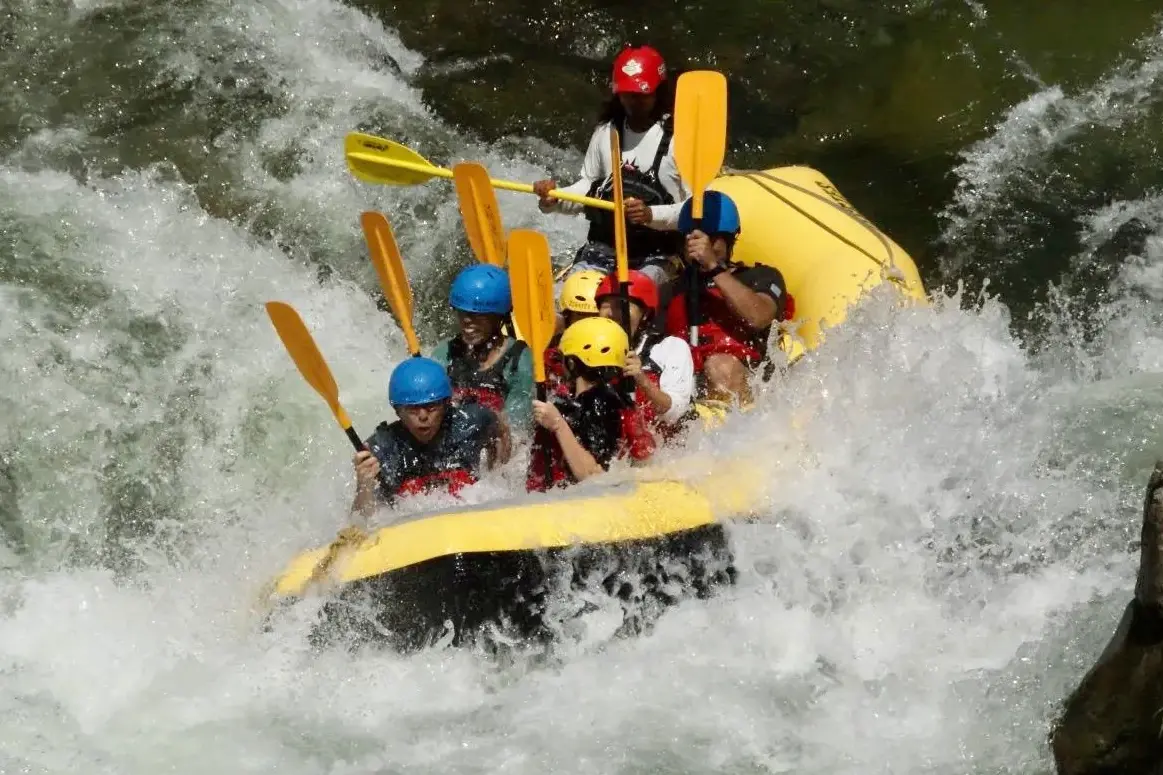 （水上）みなかみラフティングチームが激流を進む、みなかみ1日ラフティングアドベンチャーの黄色いボートとパドルでの様子。Minakami rafting team navigating intense rapids during minakami one day rafting adventure with yellow raft and paddles.