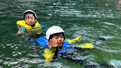 みなかみ(水上)ウォーターアドベンチャーで川遊びを楽しむ子どもたち。群馬県みなかみ町の美しい自然に囲まれた、家族向けのアウトドアアドベンチャー体験。Kids enjoying river floating at Minakami Water Adventure in Gunma, Japan, surrounded by beautiful natural scenery.