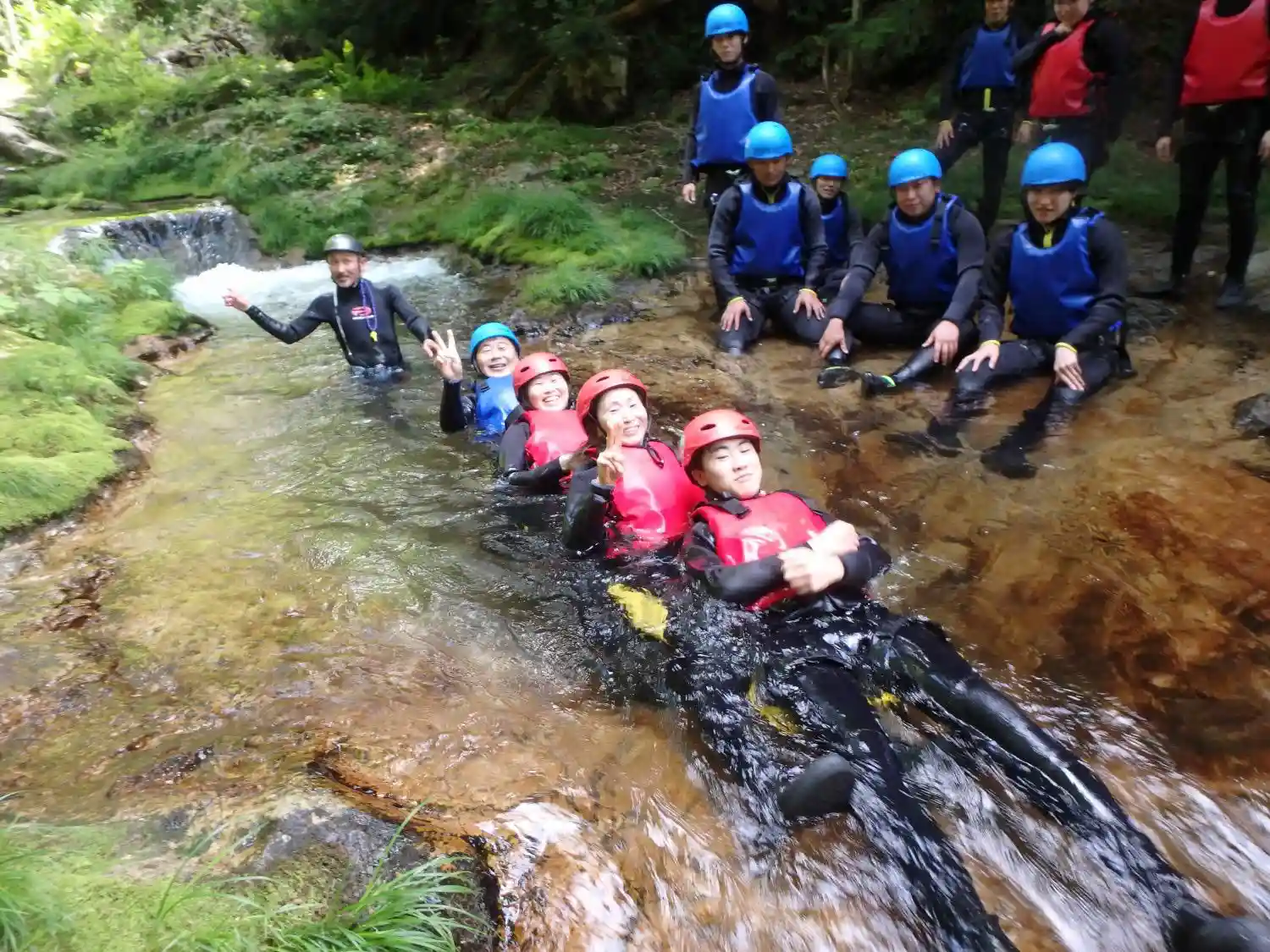 (水上)みなかみキャニオニング参加者がエキサイティングなみなかみ半日キャニオニング体験中にガイドと共に水遊びを楽しむ様子,Minakami canyoning adventurer sliding down natural waterfall chute during thrilling minakami half day canyoning tour.