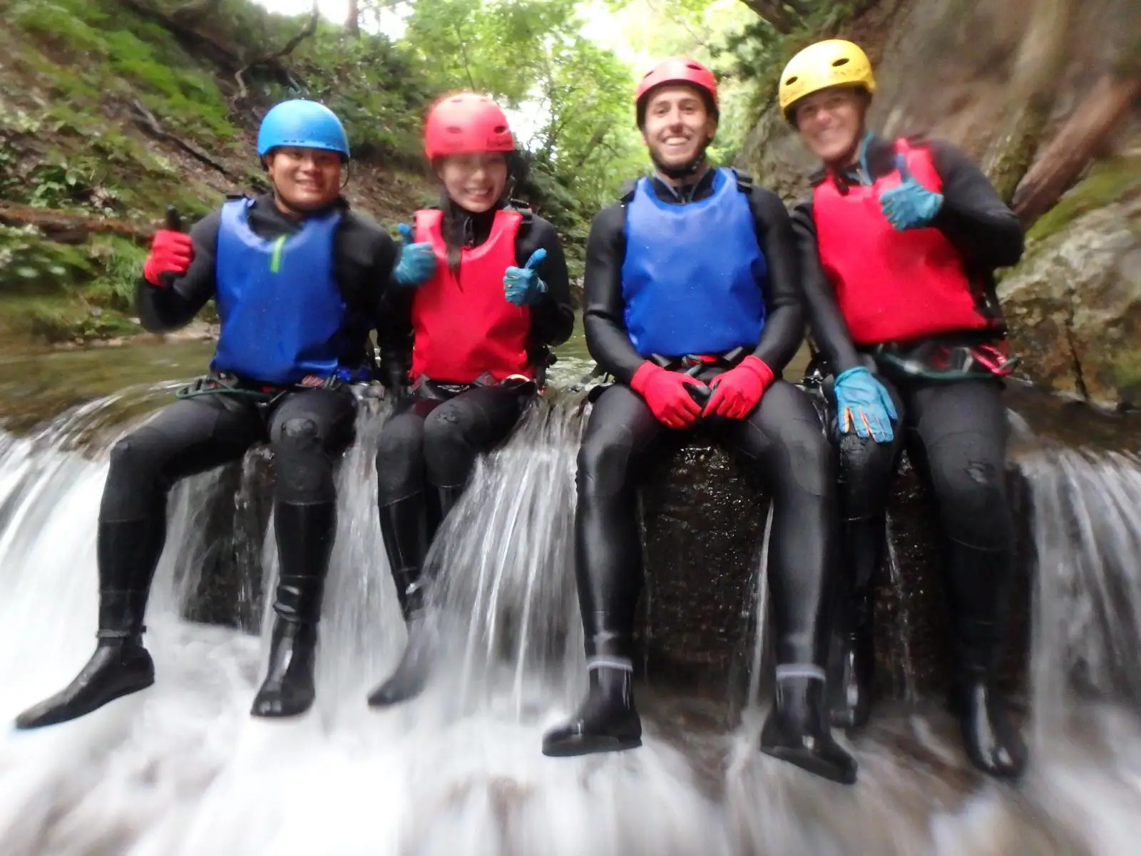 (水上)みなかみキャニオニング参加者がみなかみフォックスキャニオニングツアー中に滝の縁に座り景色の良い渓谷の景色を楽しむ, Minakami canyoning participants sitting on waterfall edge during minakami fox canyoning tour enjoying scenic canyon views