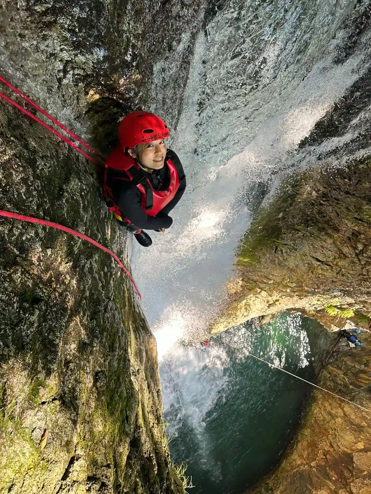 (水上)みなかみキャニオニング参加者がみなかみフォックスキャニオニングアドベンチャーツアー中に安全ロープで滝を懸垂下降, Minakami canyoning participant rappelling down waterfall with safety rope during minakami fox canyoning adventure tour.