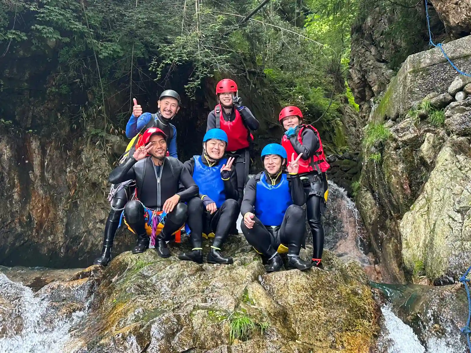 (水上)みなかみキャニオニングチームが苔むした渓谷の岩の上でみなかみフォックスキャニオニングツアーの成功完了を祝う, Minakami canyoning team celebrating successful completion of minakami fox canyoning tour on mossy canyon rocks.