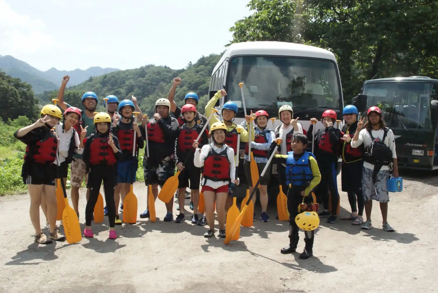 （水上）みなかみラフティンググループが山の景色の中、ツアーバスの前でパドルと安全装備を持ちみなかみ半日ラフティング冒険の準備完了。、Minakami rafting group ready for minakami half day rafting adventure with paddles and safety equipment by tour bus in mountain setting.