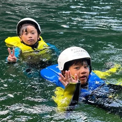 みなかみ水上ウォーターアドベンチャーで川遊びを楽しむ子どもたち。美しい自然に囲まれたみなかみのアウトドア体験。Young adventurers swimming and river floating during Minakami Water Adventure in Minakami, Japan, surrounded by beautiful nature.