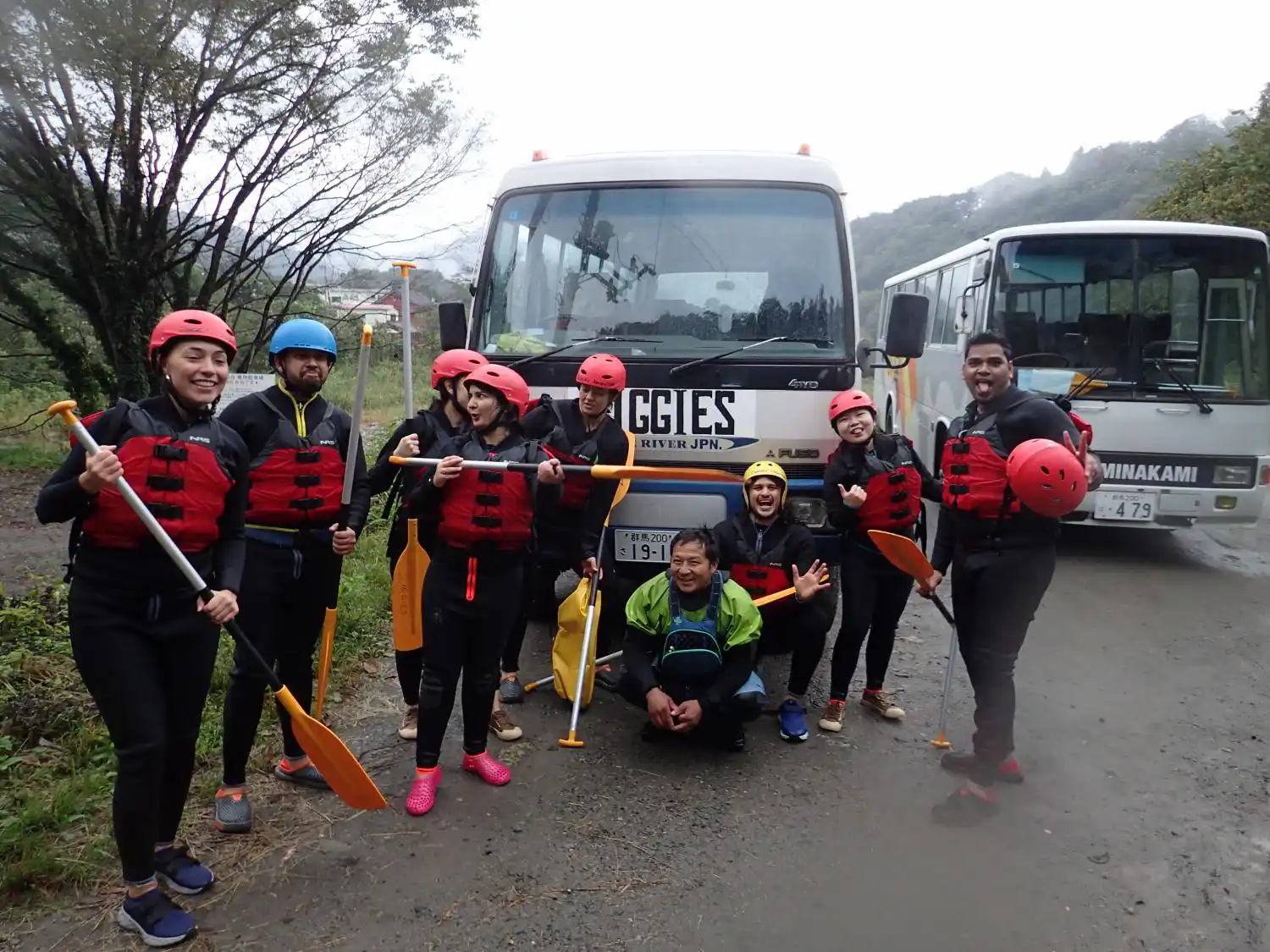 (水上)みなかみ冬ラフティンググループがツアーバスの前でパドルとガイドと共にスノーラフティングツアー完了の成功を祝う, Minakami winter rafting group celebrating successful snow rafting tour completion with paddles and guide by tour buses.