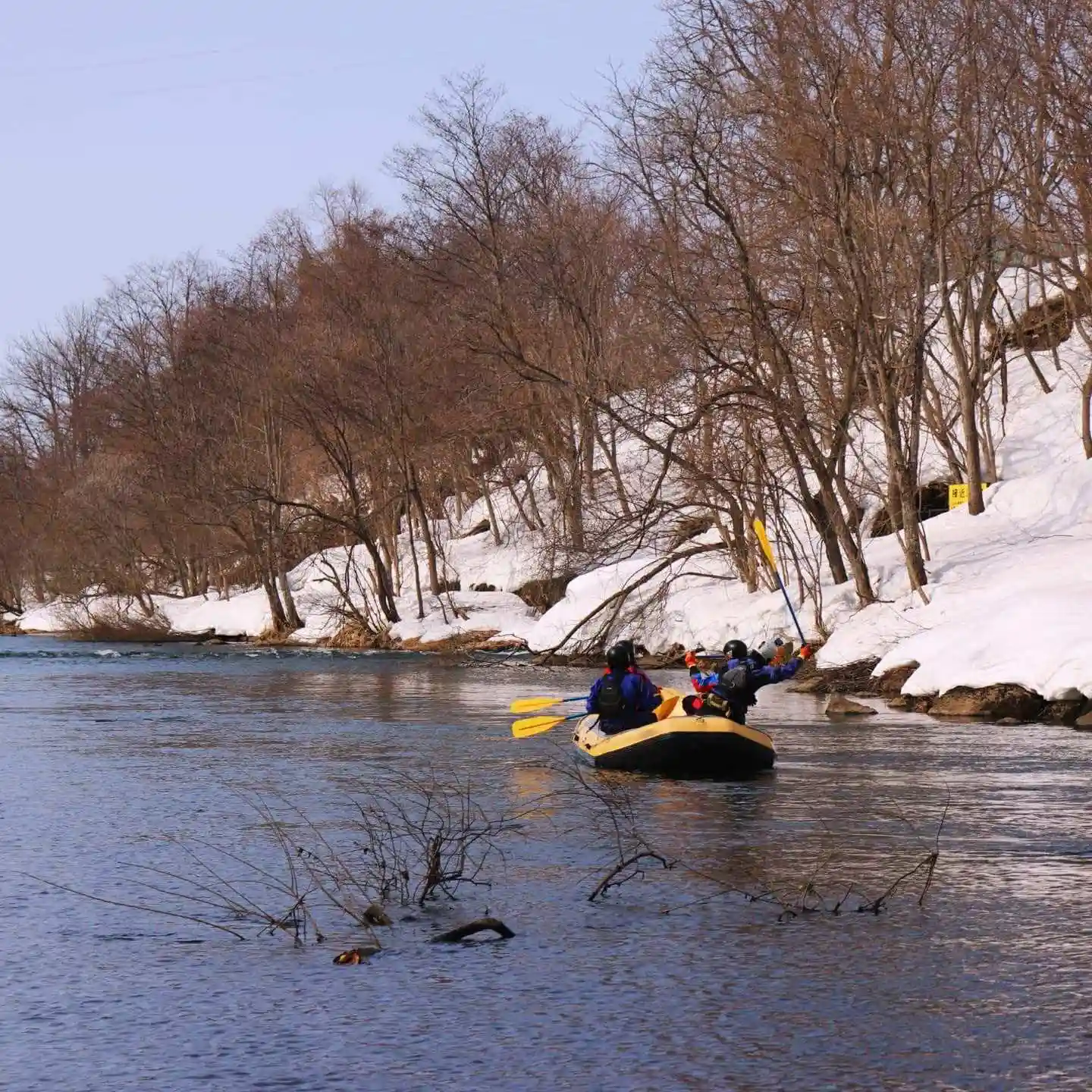 (水上)みなかみ冬ラフティングボートが穏やかなスノーラフティングの旅中に景色の良い雪に囲まれた川を漕ぐ様子, Minakami winter rafting boat paddling through scenic snow-lined river during peaceful snow rafting journey.